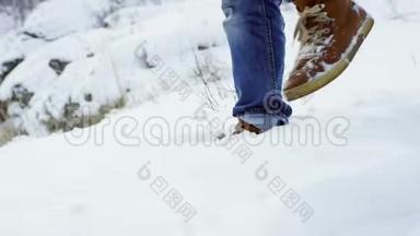 在深雪中行走的脚以慢动作射击。徒步旅行者的脚步在美丽的风景中展现。年轻人
